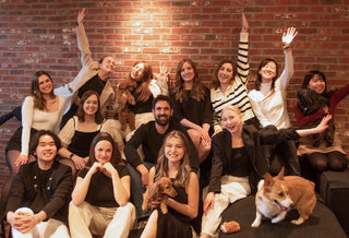 Image of the Doggos team seated across a couch and hardwood floors at the Doggos Toronto office. In various people's arms are the team's dogs. Some team members are in mid-celebratory pose.