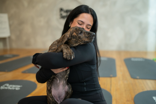 Woman in black workout clothes hugging a brindle puppy during a Puppy Sphere puppy yoga class