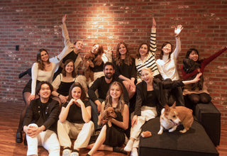 Image of the Doggos team seated across a couch and hardwood floors at the Doggos Toronto office. In various people's arms are the team's dogs. Some team members are in mid-celebratory pose.